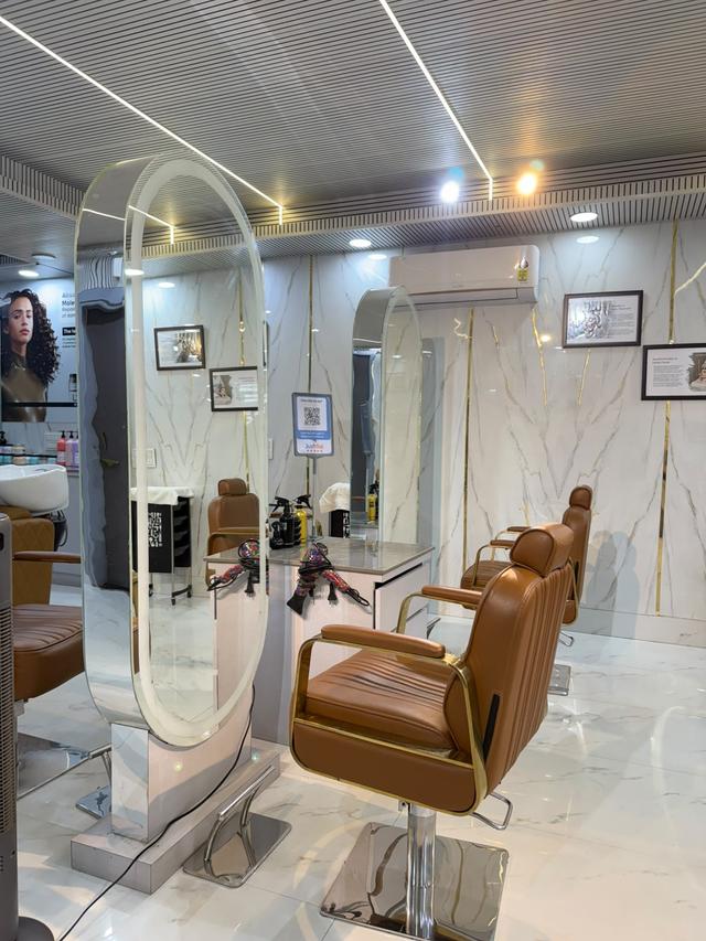 Hair styling stations with LED-lit oval mirrors and premium leather chairs in a marble-finish studio.