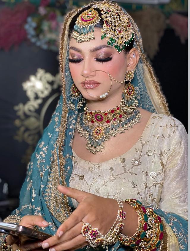 Soft-glam reception bridal makeup with sculpted cheeks and loose waves, paired with a gold lehenga and emerald jewellery